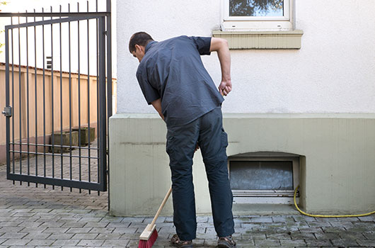 Auf dem Bild siehst du den Hausmeister mit dem Besen den Weg zu einen Hauseingang fegen.